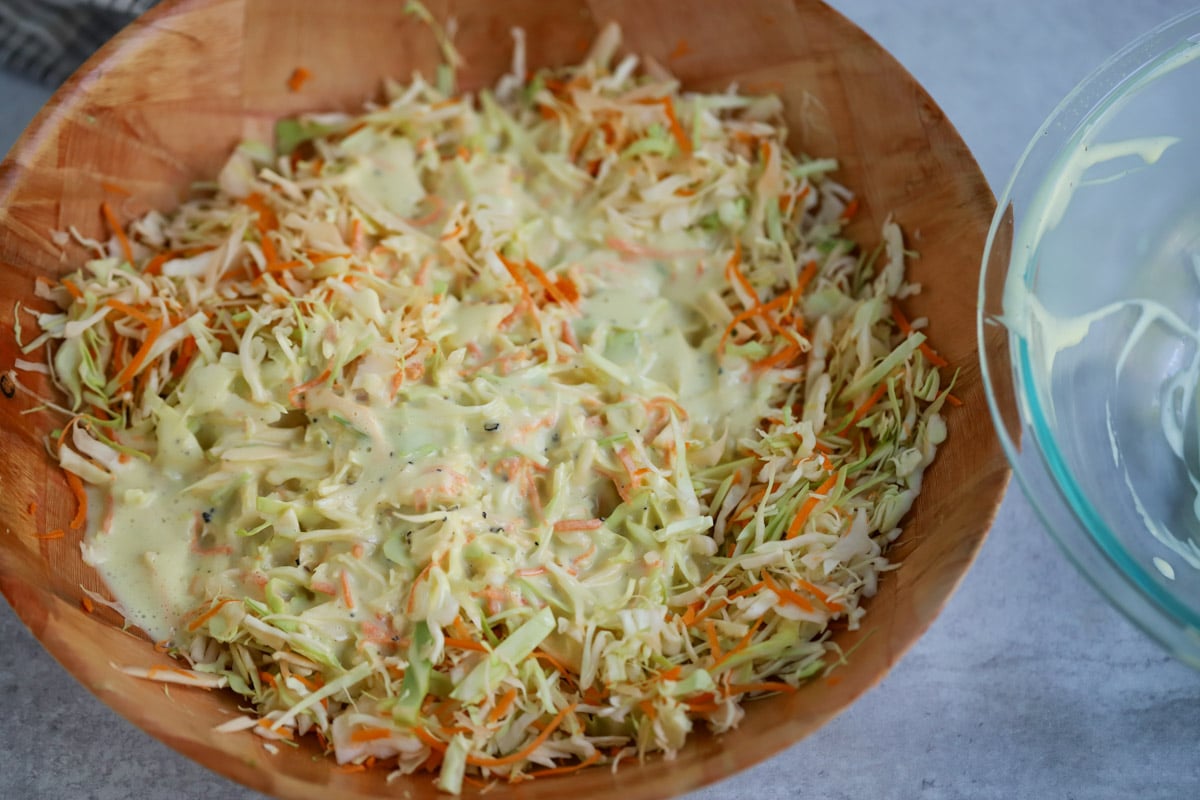 Shredded cabbage and carrots in mixing bowl with coleslaw dressing poured on top.