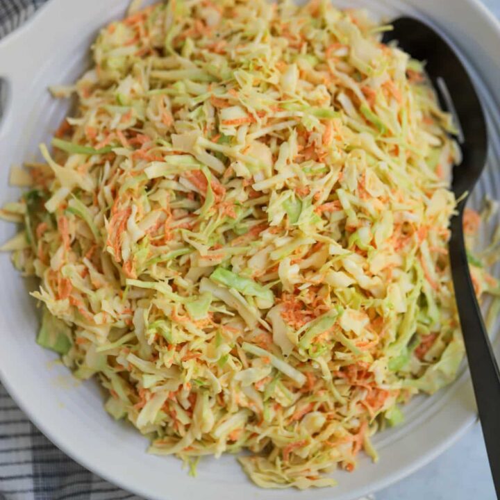 Plated coleslaw in serving dish with black spoon.