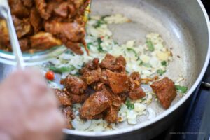 Adding lamb to the onions and garlic to saute in the pot.