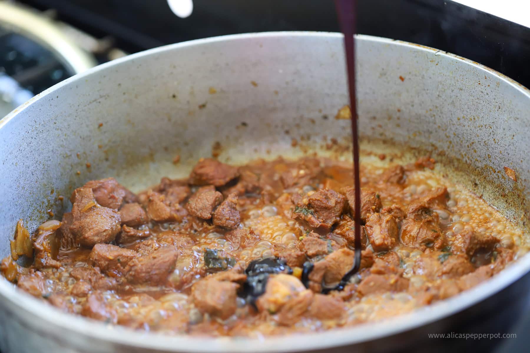 Drizzling casareep over lamb while it is cooking in the pot.