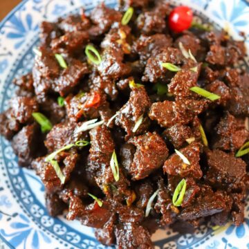 Serving dish of Guyanese casareep lamb with scallions as garnish.