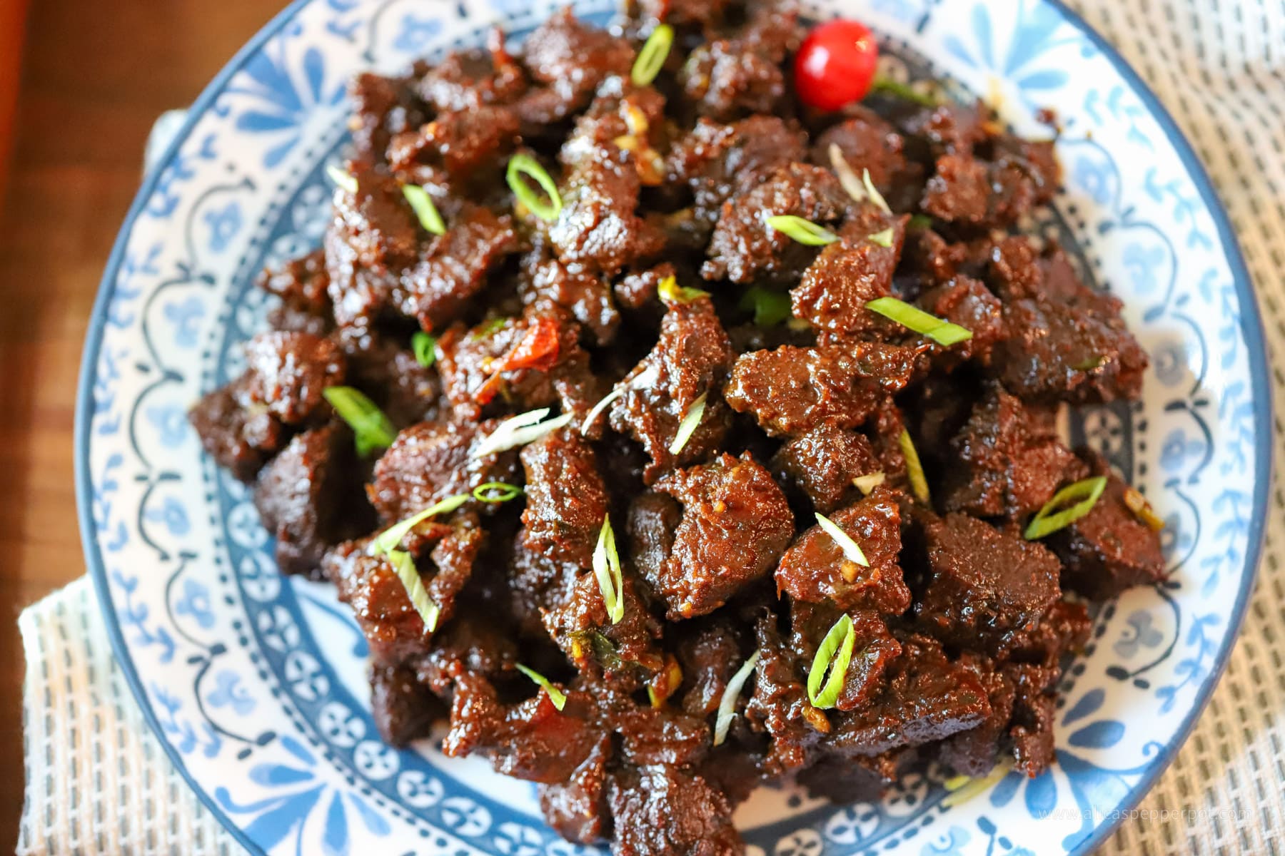 Serving dish of Guyanese casareep lamb with scallions as garnish.