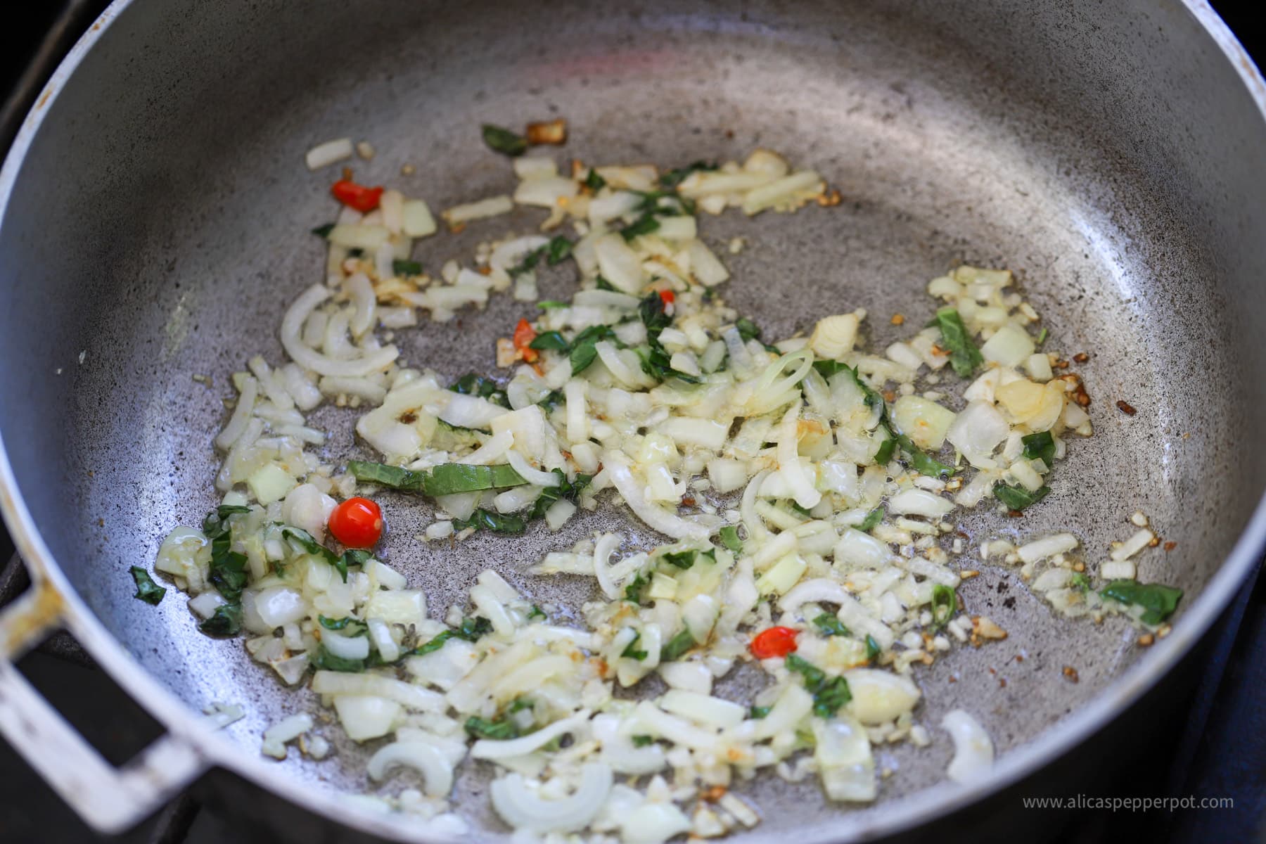 Onions, garlic, scallions, and wiri wiri pepper sauteing in pot.