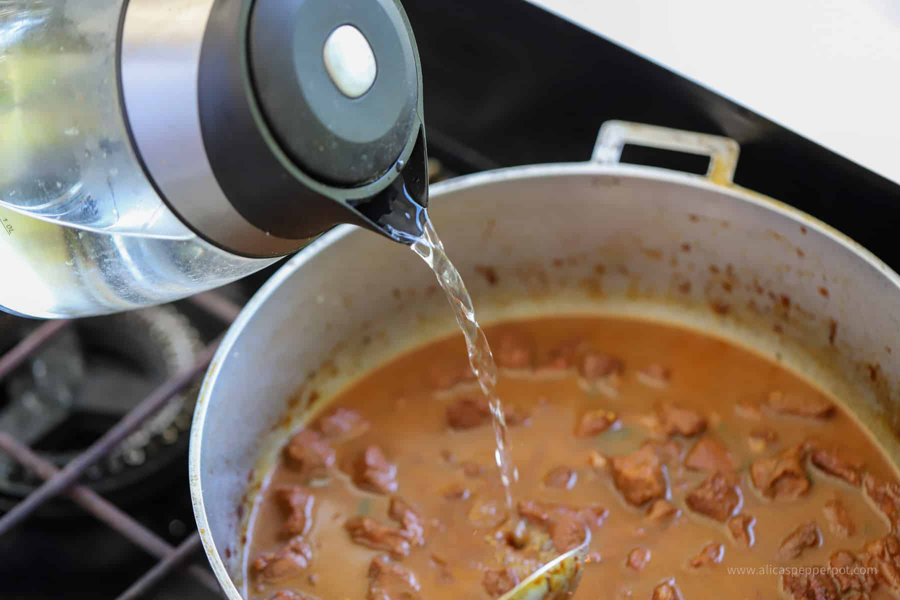 Pouring water into pot to cook casareep lamb.