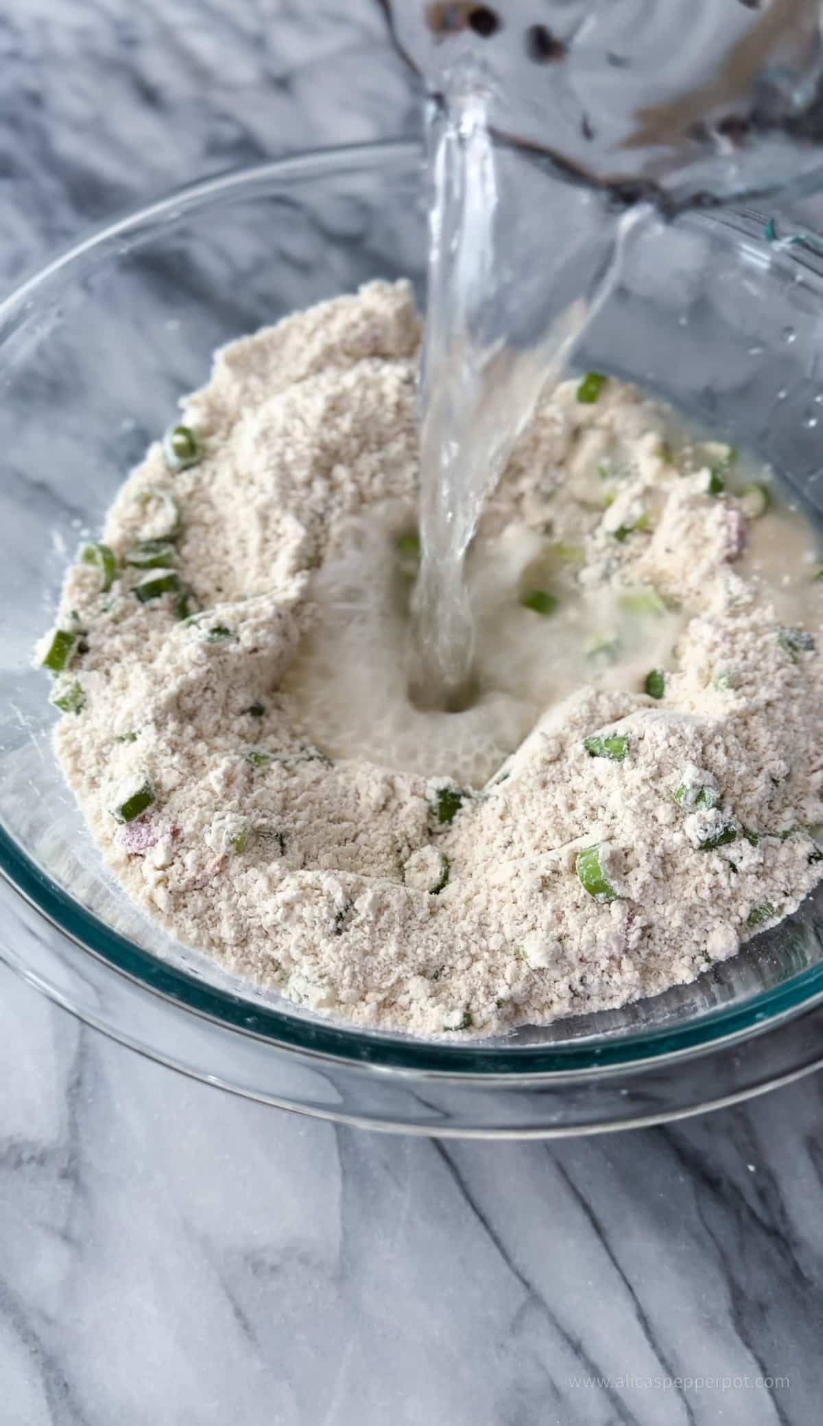 Adding water to the bowl of flour mixed with scallion and pepper