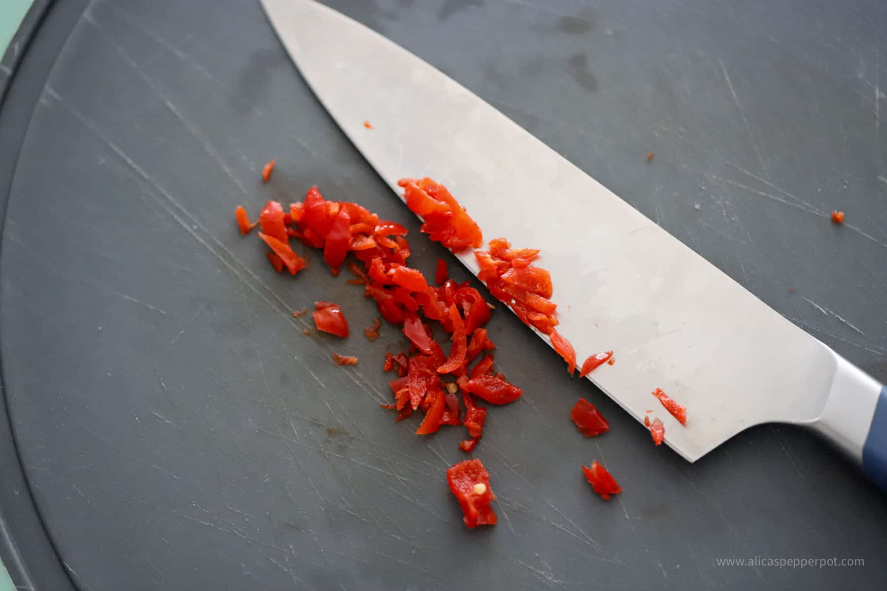 Minced wiri wiri pepper on a cutting board next to chopping knife.