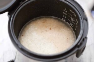 Image of rice and water in a rice cooker with lid open.