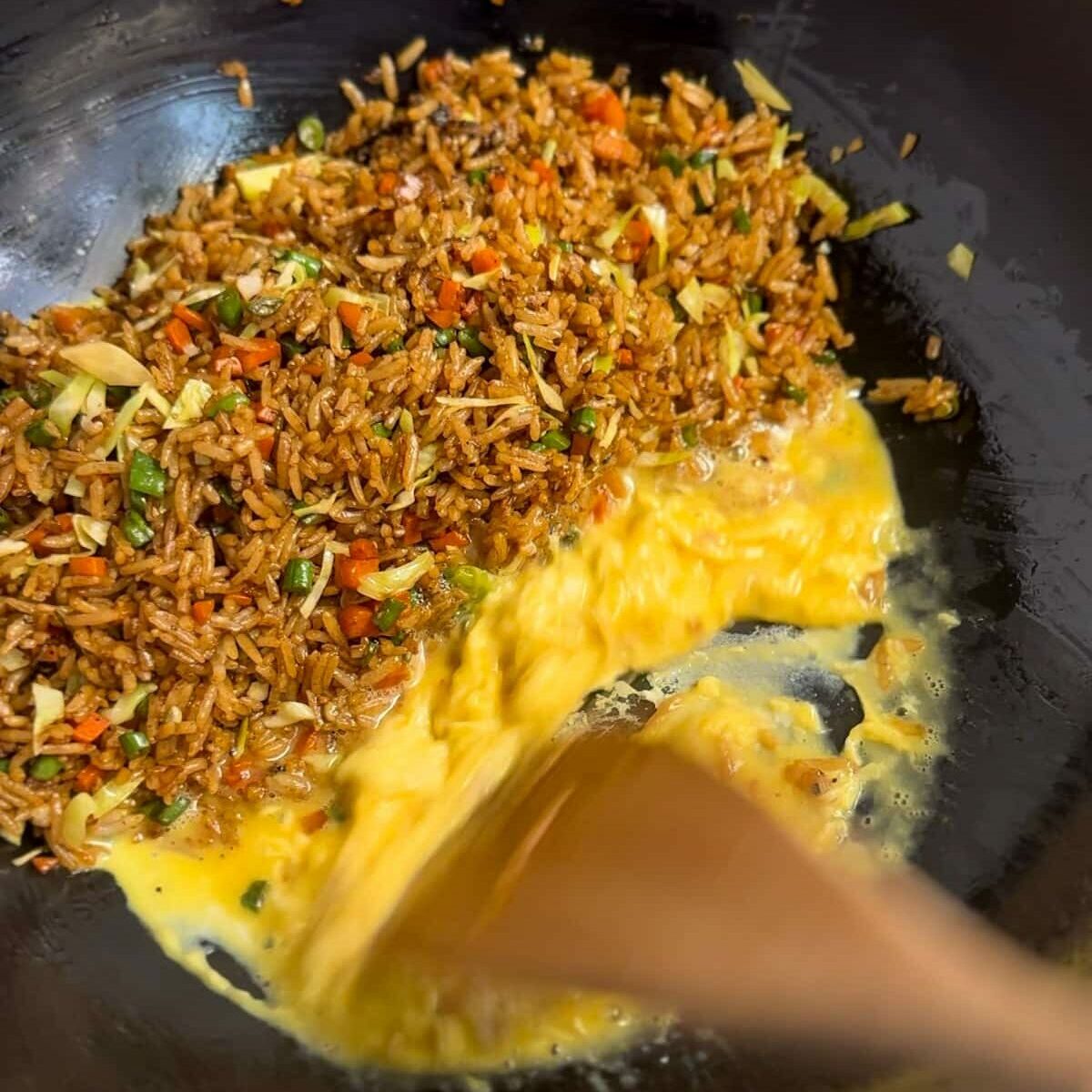 Image of egg being added to wok with fried rice pushed to the side.