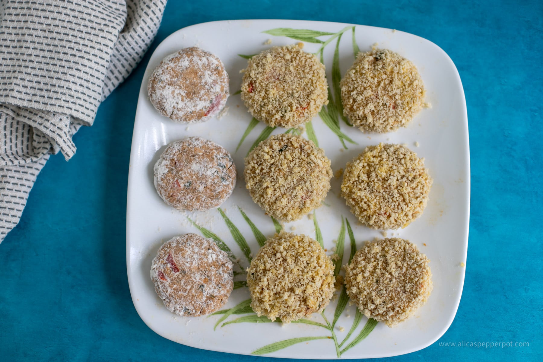 This image shows the salmon cakes before getting cooked. They are breaded and floured in a white plate.