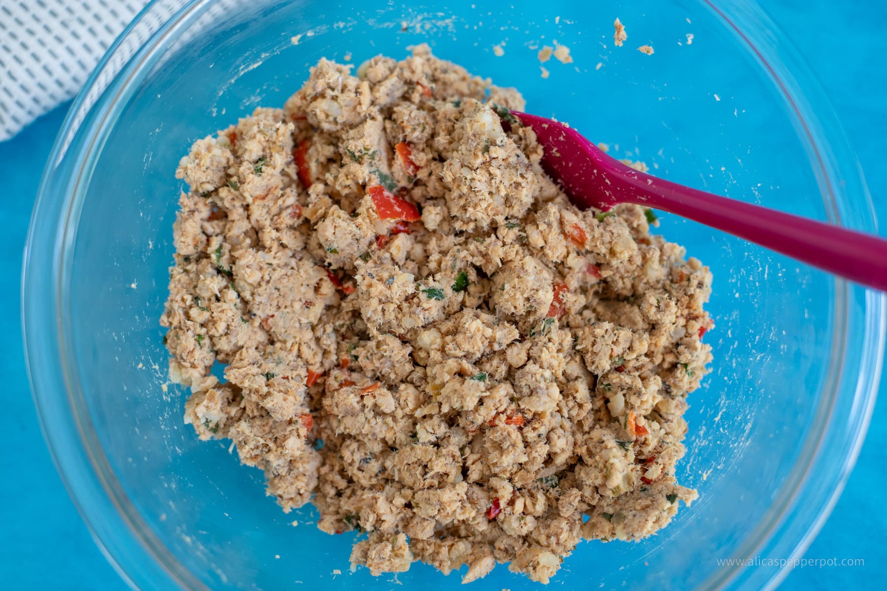 Salmon cake mixture in a clear glass mixing bowl. Mixed up with all the seasonings.