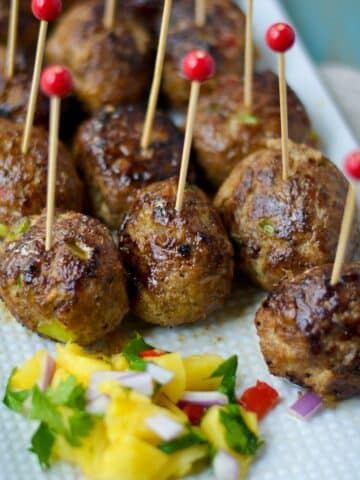 Ground chicken formed into a meatball and arranged on a white plate served as an appetizer with toothpicks in each meatball.