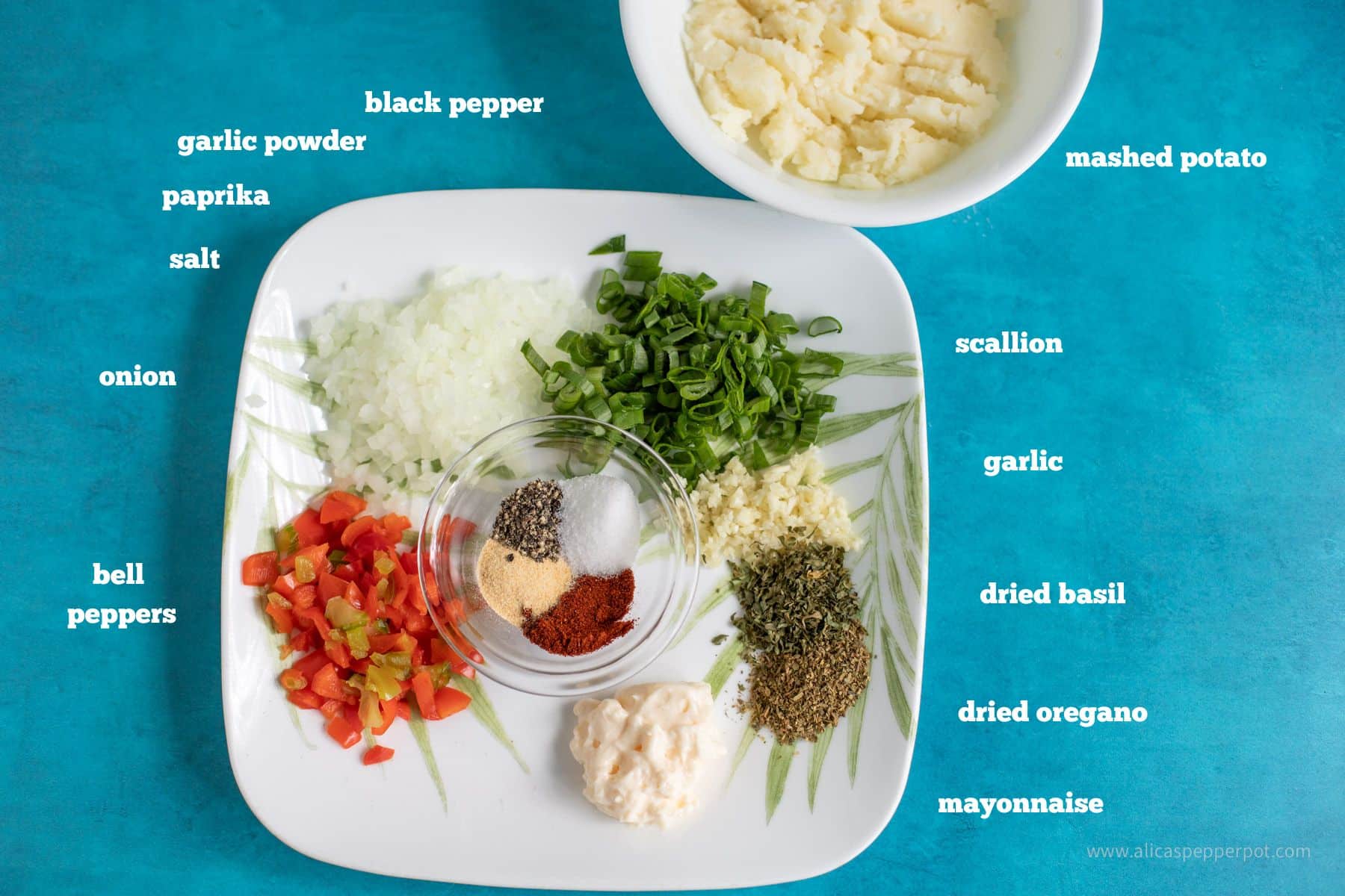 This is an image of ingredients for salmon cakes in a white plate on a blue background. it includes black pepper garlic powder paprika salt onion bell peppers mashed potato scallion garlic dried basil oregano and mayonnaise