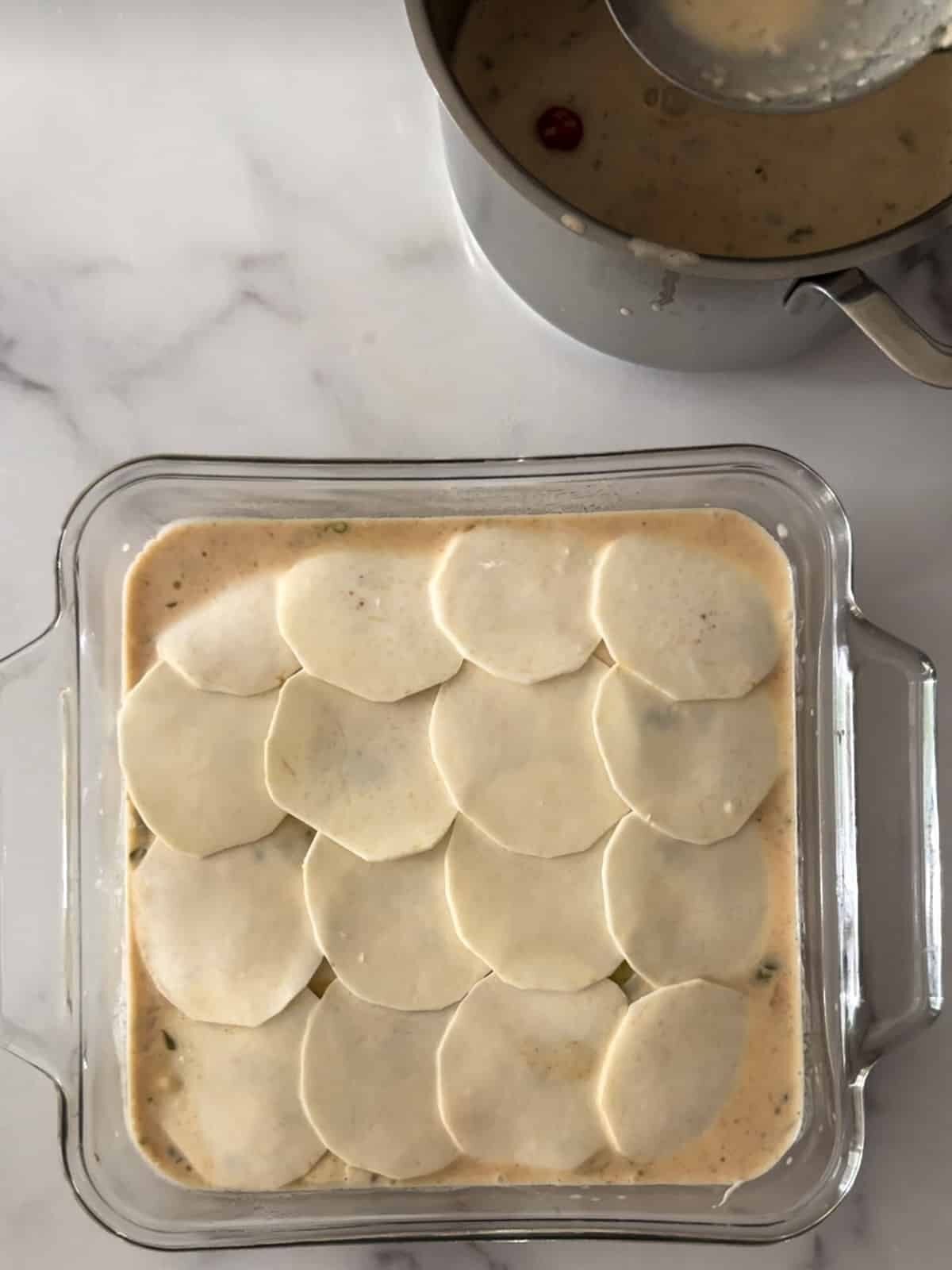 Layered scalloped eddoe with pot of coconut milk sauce on the side