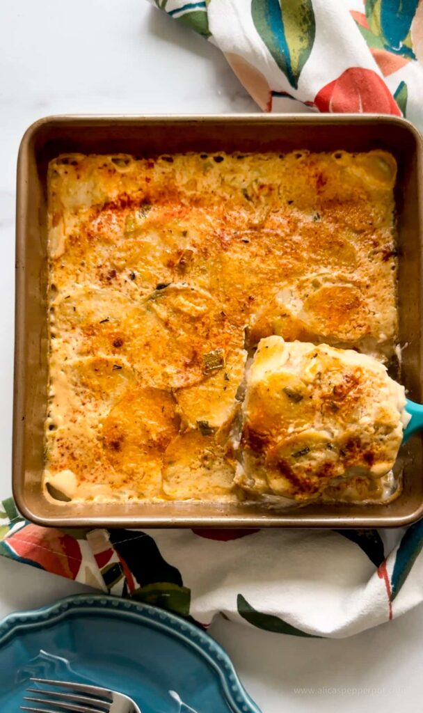 Baked scalloped Eddoe in a metal pan with some eddoe being scooped out.