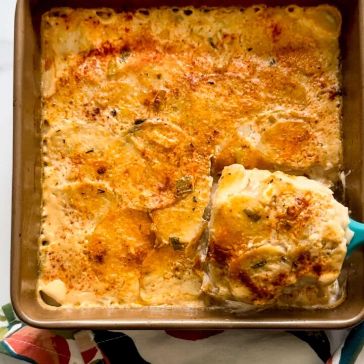 Baked scalloped Eddoe in a metal pan with some eddoe being scooped out.