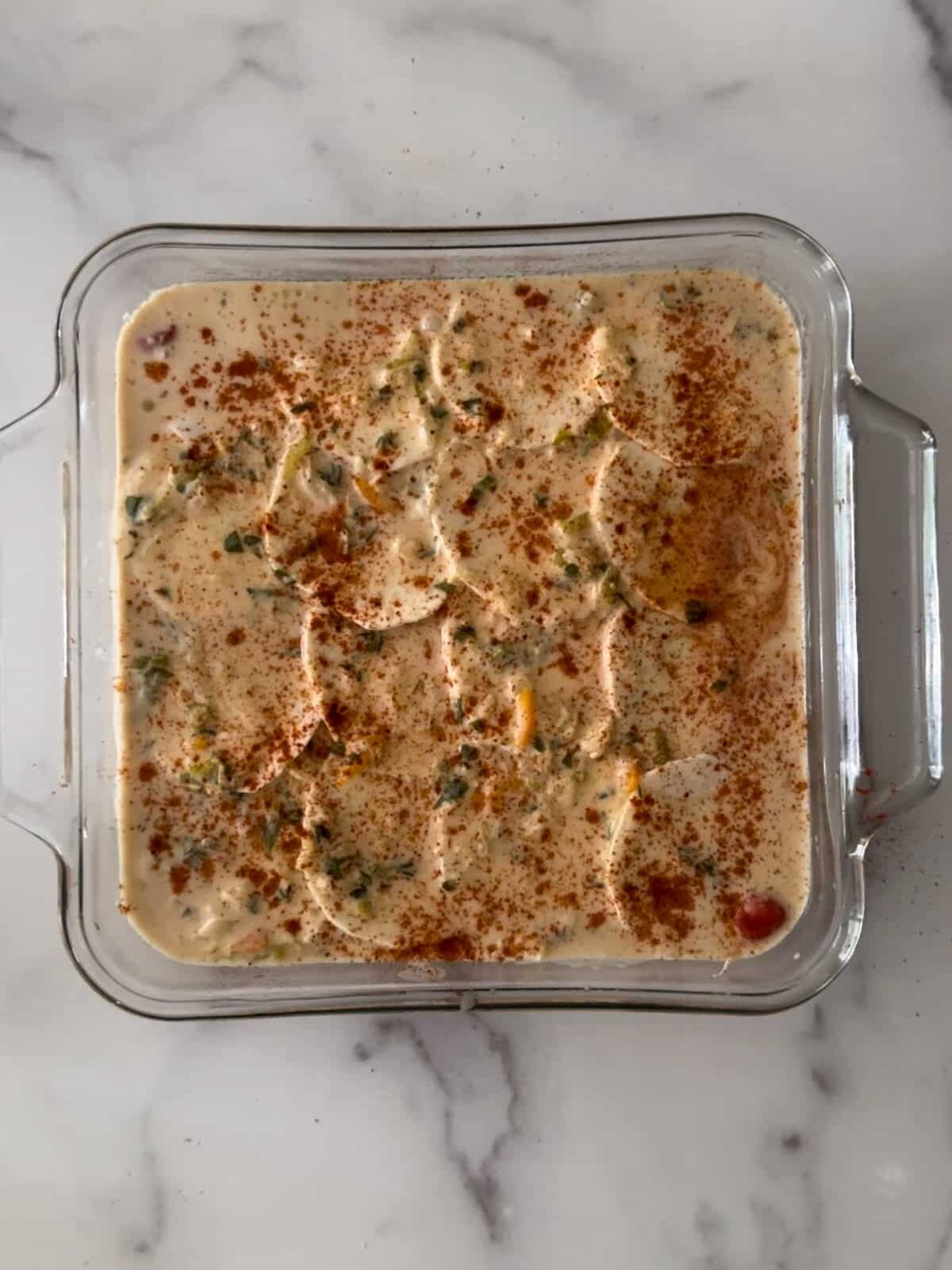 Scalloped eddoe in coconut milk sauce in a glass dish before going into the oven.