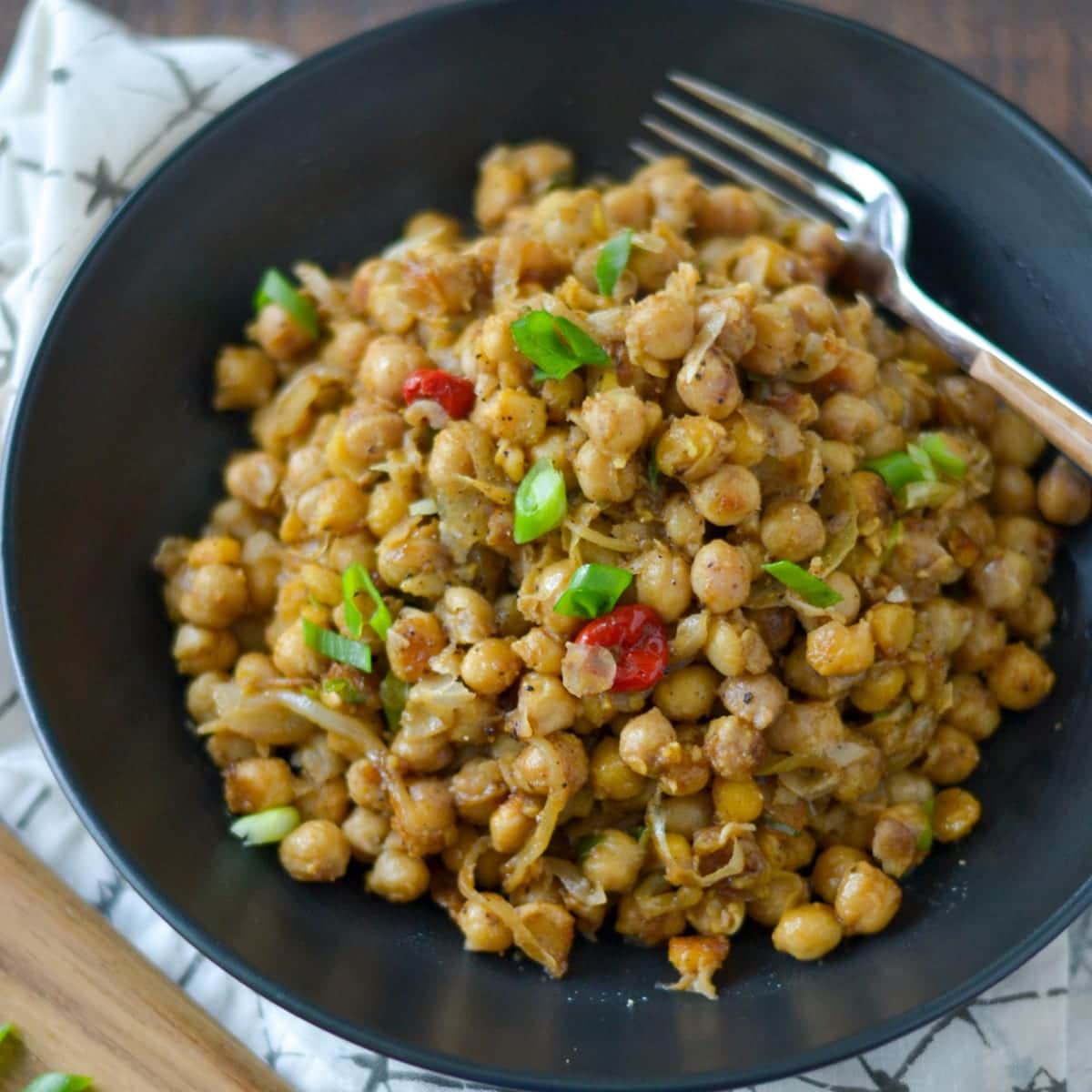 fried channa in a black bowl with a fork and wiri wiri pepper