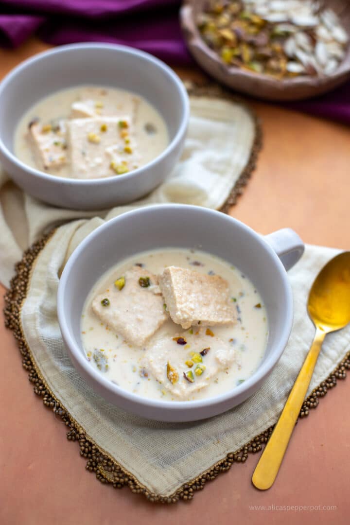 Rasmalai made with ricotta cheese plated in a two grey bowls on an ivory napkin with a gold spoon next to it. A dessert for Diwali.